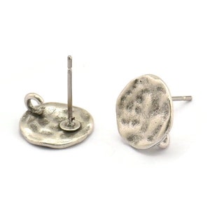 May include: A pair of silver-toned earring posts with a textured, round disc design. The posts are made of metal and have a loop on the back for attaching to earrings.
