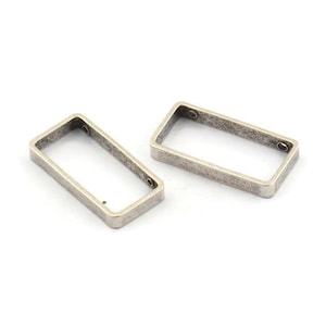 Puede incluir: Dos anillos de salto rectangulares de metal plateado. Los anillos están abiertos y tienen un acabado ligeramente desgastado.