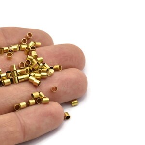 Może przedstawiać: Zbliżenie na dłoń trzymającą stos małych, złotych metalowych rurek. Rurki mają średnicę około 6 mm i długość 12 mm.