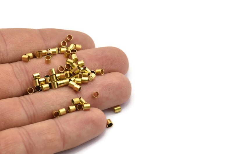 Może przedstawiać: Zbliżenie na dłoń trzymającą stos małych, złotych metalowych rurek. Rurki mają średnicę około 6 mm i długość 12 mm.