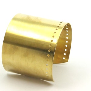 K&ouml;nnte beinhalten: Ein goldfarbenes Metall-Armband mit einer Reihe kleiner L&ouml;cher am Rand.