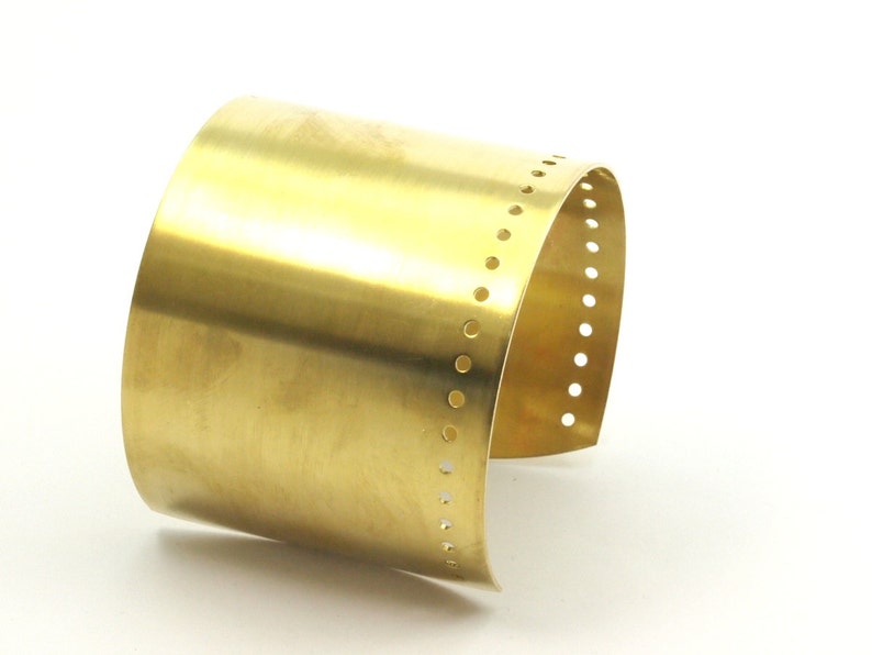 K&ouml;nnte beinhalten: Ein goldfarbenes Metall-Armband mit einer Reihe kleiner L&ouml;cher am Rand.