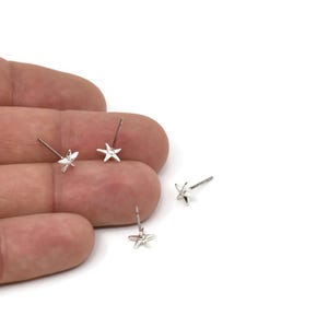 May include: Three silver star-shaped stud earrings on a hand. The earrings are small and delicate.