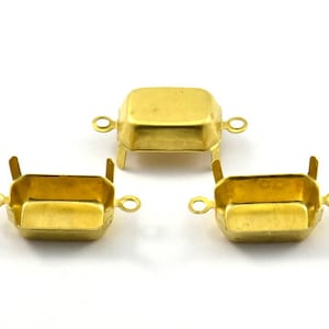 Peut inclure: Trois montures métalliques dorées pour sertir des pierres. Chaque monture a deux boucles sur les côtés et une forme carrée.