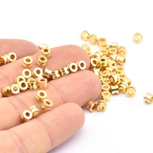 K&ouml;nnte beinhalten: Ein gro&szlig;er Haufen goldfarbener Metallperlen, von denen einige in einer Hand gehalten werden. Die Perlen sind rund und haben eine glatte Oberfl&auml;che.