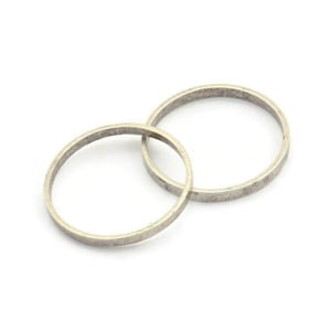 May include: Two silver wedding bands, one slightly larger than the other, are intertwined and lying on a white surface.