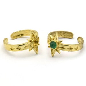 May include: Two gold adjustable rings with a starburst design. One ring has a green gemstone in the center of the starburst.