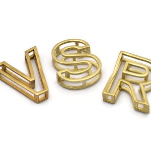 Pu&ograve; includere: Lettere in metallo color oro che compongono la parola "VSR". Ogni lettera &egrave; realizzata con una singola linea continua di metallo, creando un design vuoto a telaio aperto.