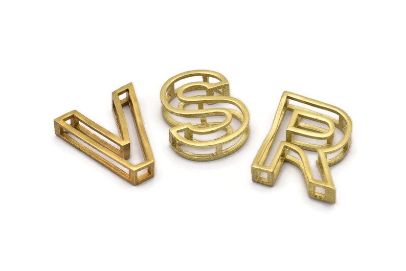 Pu&ograve; includere: Lettere in metallo color oro che compongono la parola "VSR". Ogni lettera &egrave; realizzata con una singola linea continua di metallo, creando un design vuoto a telaio aperto.