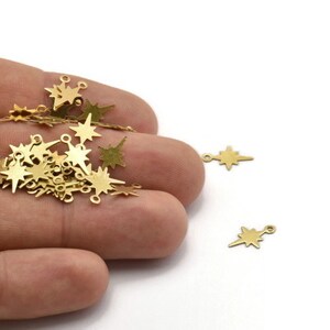May include: A pile of gold-colored metal star charms with jump rings. The charms are in the shape of a star with a pointed tip.