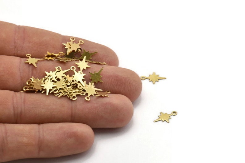 May include: A pile of gold-colored metal star charms with jump rings. The charms are in the shape of a star with a pointed tip.