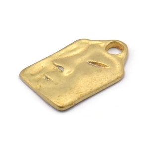 Puede incluir: Encanto de metal dorado con un diseño de rostro estilizado. El encanto tiene un pequeño bucle en la parte superior para sujetarlo a joyas u otras manualidades.