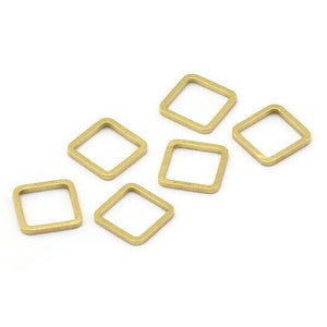 Puede incluir: Seis pequeños hallazgos de joyería de metal dorado, de forma cuadrada, están dispersos sobre un fondo blanco. Cada hallazgo tiene un centro hueco y abierto, y un acabado liso y mate. Estos hallazgos son ideales para la fabricación de joyas.