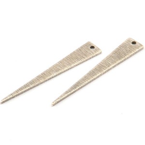 Puede incluir: Dos abalorios de metal de color plateado en forma de triángulo con una superficie texturizada y un pequeño agujero en la parte superior.