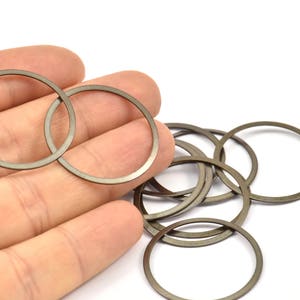 May include: A close-up of a hand holding a set of 10 silver-colored metal rings. The rings are stacked and overlapping, creating a circular pattern.