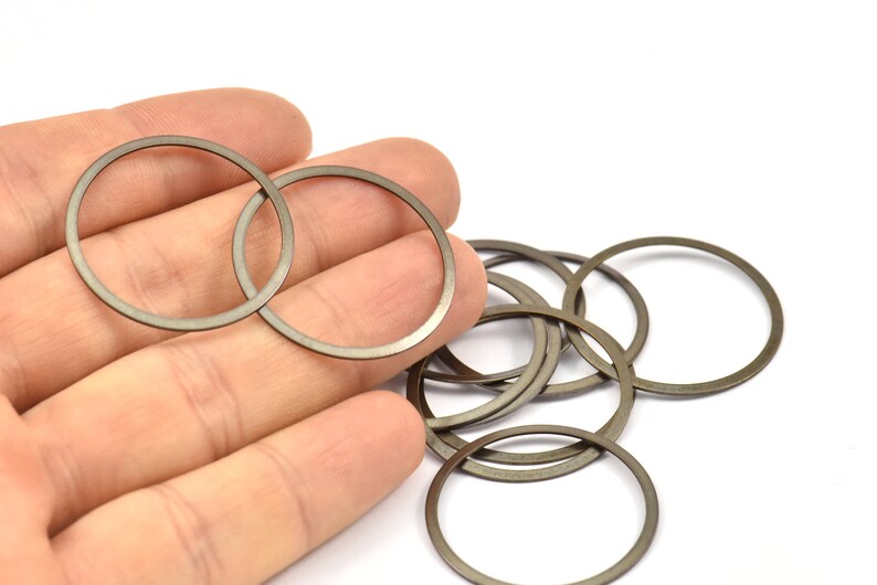 May include: A close-up of a hand holding a set of 10 silver-colored metal rings. The rings are stacked and overlapping, creating a circular pattern.