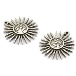 May include: Two silver-toned sun charms with a face on each. The sun has a circular face with rays extending out from the face.