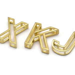Pu&ograve; includere: Tre ciondoli in metallo color oro a forma delle lettere X, K e J. Le lettere sono cave e hanno un design geometrico.