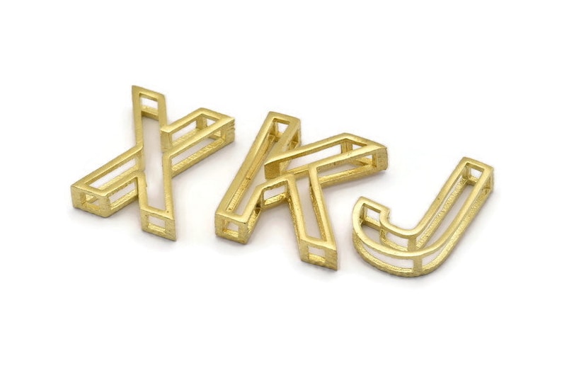 Pu&ograve; includere: Tre ciondoli in metallo color oro a forma delle lettere X, K e J. Le lettere sono cave e hanno un design geometrico.