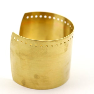 K&ouml;nnte beinhalten: Ein goldfarbenes Metall-Armband mit einer Reihe kleiner L&ouml;cher am oberen Rand.