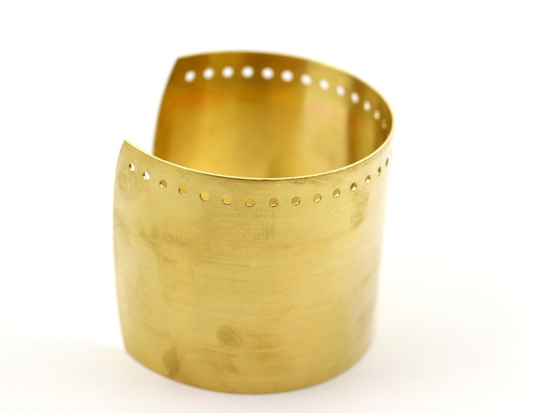 K&ouml;nnte beinhalten: Ein goldfarbenes Metall-Armband mit einer Reihe kleiner L&ouml;cher am oberen Rand.