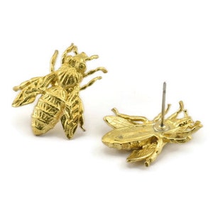 May include: A pair of gold bee stud earrings. The bee is detailed with textured wings and a body.