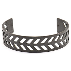Könnte beinhalten: Ein schwarzes Metall-Armband mit einem durchbrochenen Chevron-Muster.
