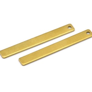 Può includere: Due ciondoli a barra in metallo color oro con un foro nella parte superiore per l'appeso. Le barre sono lisce e hanno una superficie leggermente testurizzata.