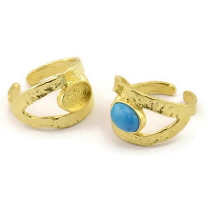 May include: Two gold rings with a textured finish. One ring has a turquoise stone set in the center, while the other ring has a blank setting.