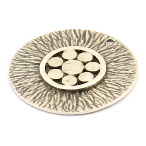 May include: Silver pendant with a textured circular design and a smaller circular cutout in the center. The cutout features a stylized flower design with seven circles.