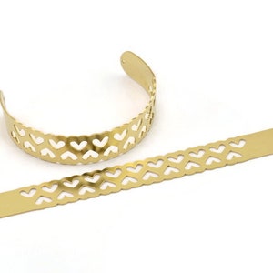 Puede incluir: Dos bandas de metal dorado con un diseño de corte en forma de corazón. Las bandas son planas y tienen un acabado liso.