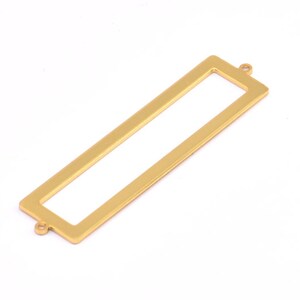 May include: Gold-toned metal rectangle frame with two jump rings. The frame is hollow and can be used to hold a small piece of paper or fabric.