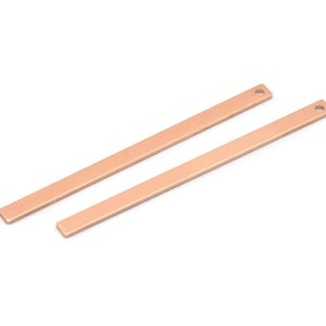 May include: Two rose gold metal bar charms with a hole at the top. The bars are flat and rectangular.