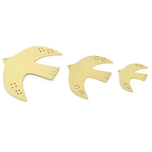 Peut inclure: Trois colombes en bois en vol, peintes d'une couleur jaune pâle. Les colombes sont disposées en rang, la plus grande devant et la plus petite derrière.