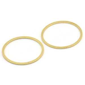 Puede incluir: Dos anillos de metal de color dorado, cada uno con una forma circular lisa. Los anillos están colocados planos sobre una superficie blanca.