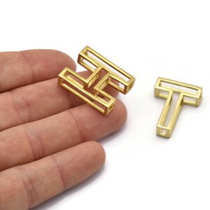 Pu&ograve; includere: Due ciondoli in metallo color oro, uno a forma della lettera H e l'altro a forma della lettera T. I ciondoli sono vuoti e hanno un design geometrico.
