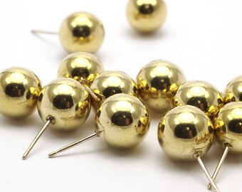 May include: A group of gold-colored metal ball earrings. The earrings are round and have a shiny finish. They are scattered on a white surface.