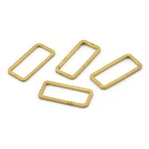 May include: Four gold-colored metal rectangular rings, also known as jump rings, are arranged on a white surface.