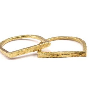 Könnte beinhalten: Zwei goldene, gehämmerte Metallringe, jeder mit einer quadratischen Form und einer abgerundeten Oberseite. Die Ringe sind übereinander gestapelt.