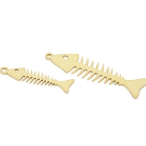 May include: Two gold-colored fish bone charms, one larger than the other, isolated on a white background.