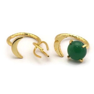 May include: Two gold rings with a crescent moon design. One ring has a green gemstone in the center.