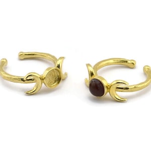 Puede incluir: Dos anillos de oro con un diseño de triple luna. Un anillo tiene un engaste redondo para una piedra, el otro tiene una piedra roja oscura engastada en el engaste.