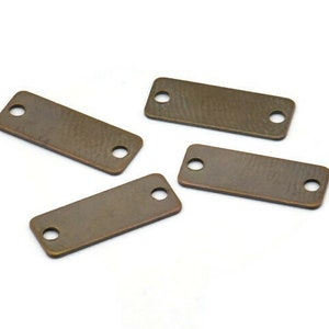 May include: Four antique gold-toned metal rectangular tags with two holes each. The tags are smooth and have a slightly textured surface.