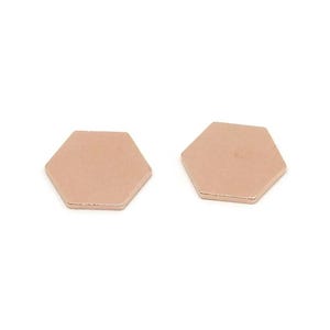 May include: Two rose gold hexagon-shaped metal pieces. The pieces are flat with a smooth surface and a metallic sheen. The shapes are identical and are set against a white background.