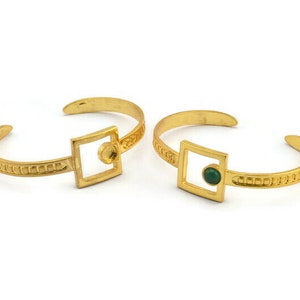 May include: Two gold bracelets with square-shaped accents. One bracelet has a green stone in the center of the square, while the other has a plain square.