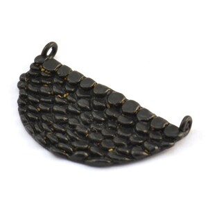 May include: A dark, textured metal pendant in a crescent shape. The surface is covered in a scale-like pattern. The pendant has a small loop at each end for attaching to a chain or other jewelry component.