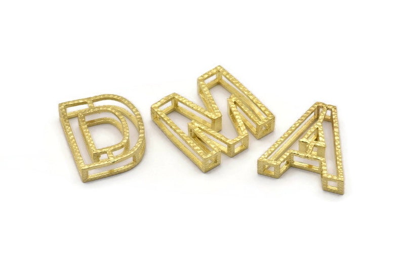 Pu&ograve; includere: Lettere in metallo color oro che compongono la parola "DNA". Ogni lettera &egrave; composta da pi&ugrave; strati di metallo, creando un effetto tridimensionale.