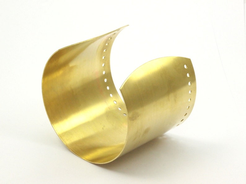 K&ouml;nnte beinhalten: Ein goldfarbenes Metall-Armband mit glatter, polierter Oberfl&auml;che. Das Armband hat eine Reihe kleiner L&ouml;cher entlang der Kante.