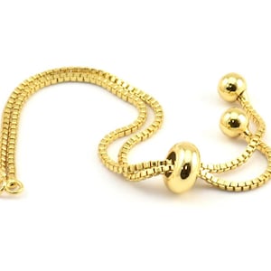 Peut inclure: Un bracelet en chaîne dorée avec un fermoir coulissant et trois perles rondes. La chaîne est composée de petits maillons carrés.