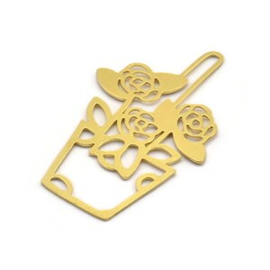 Może przedstawiać: Złoty metalowy zakładka w kształcie doniczki z trzema różami. Zakładka jest wycięta i ma delikatny wzór.